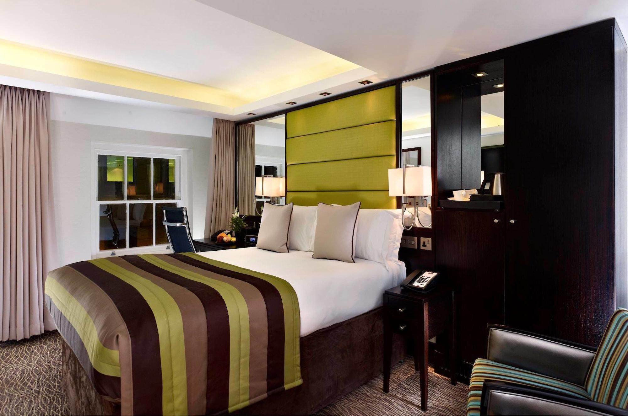 Montcalm Brewery Townhouse Hotel Londra Exterior foto The photo shows a modern hotel room featuring a large bed with a striped comforter in shades of green, brown, and cream. The bed is adorned with several decorative pillows. Behind the bed, there is a contemporary headboard with a green panel design. 