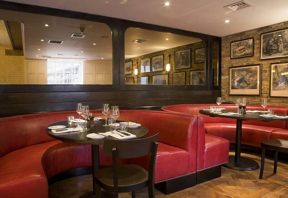 Montcalm Brewery Townhouse Hotel Londra Exterior foto The image shows the interior of a restaurant featuring a warm and inviting atmosphere. There are several round tables surrounded by black chairs, with red, upholstered booths lining the walls. The decor includes framed artwork hanging on the walls, a