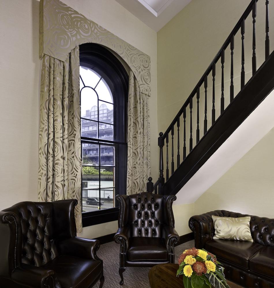 Montcalm Brewery Townhouse Hotel Londra Exterior foto The photo shows a cozy interior space featuring two elegant leather armchairs placed near a large, ornate window with arched top and decorative curtains. The wall is painted in a muted color, enhancing the warmth of the room. A staircase with black s