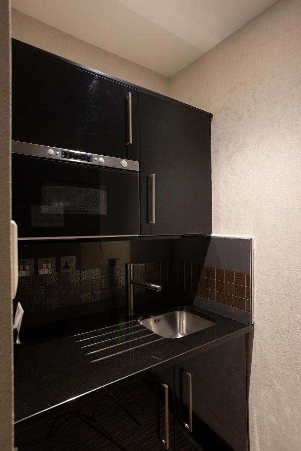 Montcalm Brewery Townhouse Hotel Londra Exterior foto The photo shows a modern kitchen setup with a dark color scheme. It features:

- A built-in microwave oven situated above a countertop.
- A sleek black cabinet beneath the microwave, which likely stores kitchen items.
- A stainless steel sink placed 