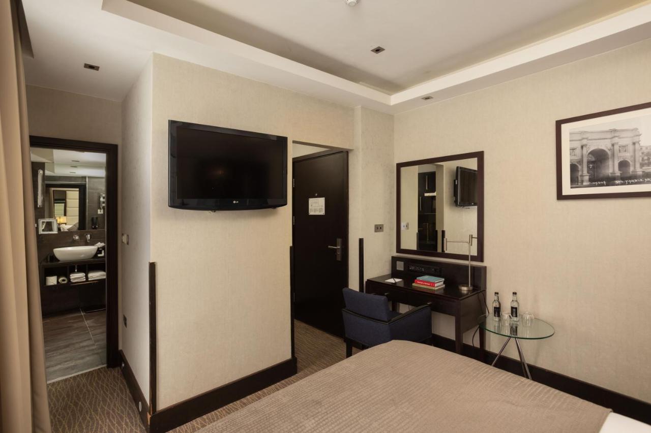 Montcalm Brewery Townhouse Hotel Londra Exterior foto The photo shows a hotel room featuring a double bed with a neutral-colored bedspread. On one wall, there is a flat-screen TV mounted. Adjacent to the bed, there is a stylish desk with a chair and a small glass table. A mirror is positioned above the 