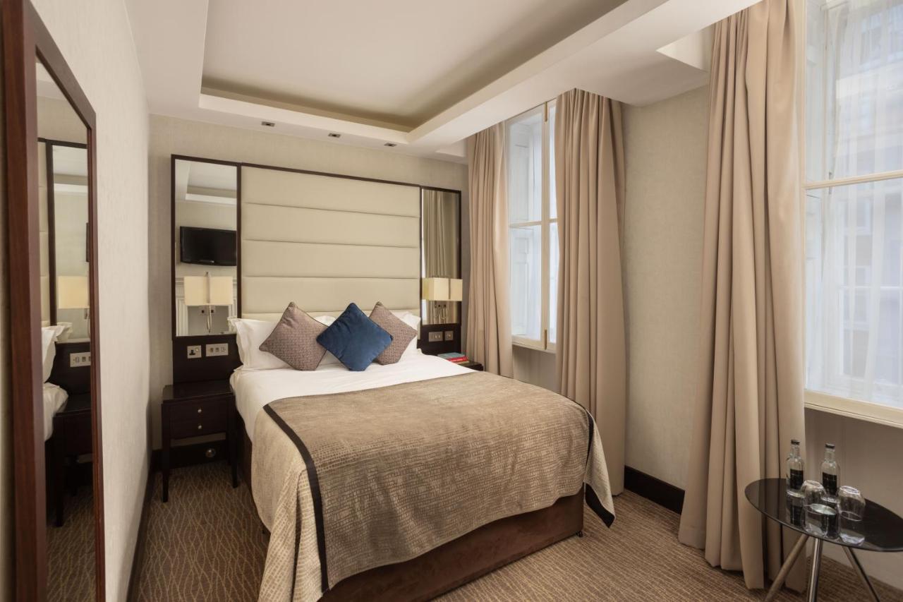 Montcalm Brewery Townhouse Hotel Londra Exterior foto The photo shows a cozy hotel bedroom. The room features a neatly made double bed with a beige bedspread and decorative pillows, including a blue one. There are bedside tables on either side of the bed with lamps. The walls are painted in a soft color
