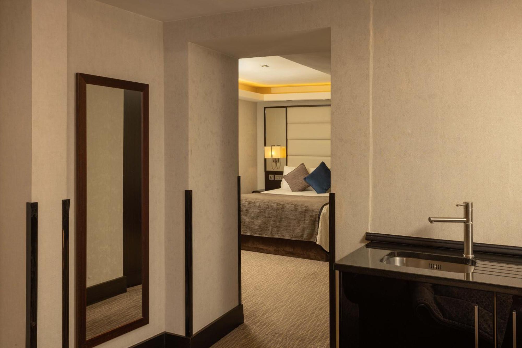 Montcalm Brewery Townhouse Hotel Londra Exterior foto The photo shows an interior space that appears to be part of a hotel room or suite. There is a doorway leading into a bedroom area, where a bed with decorative pillows is visible. In the foreground, there's a tall mirror on the left side and a small 