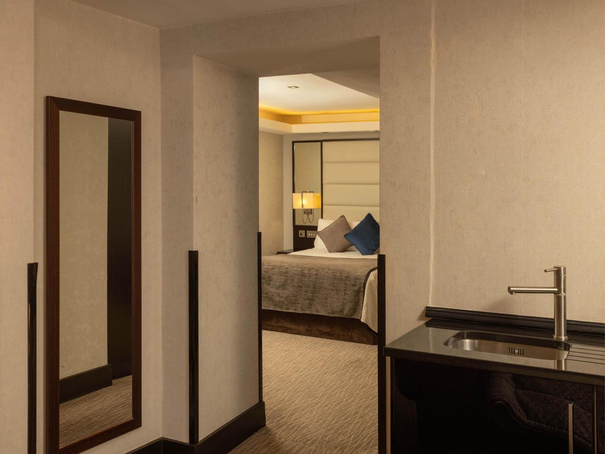 Montcalm Brewery Townhouse Hotel Londra Exterior foto The photo shows an interior space that appears to be a hotel room or a suite. There is a doorway leading to a bedroom visible in the background, where a bed with decorative pillows can be seen. To the side, there is a small wet bar or kitchenette are