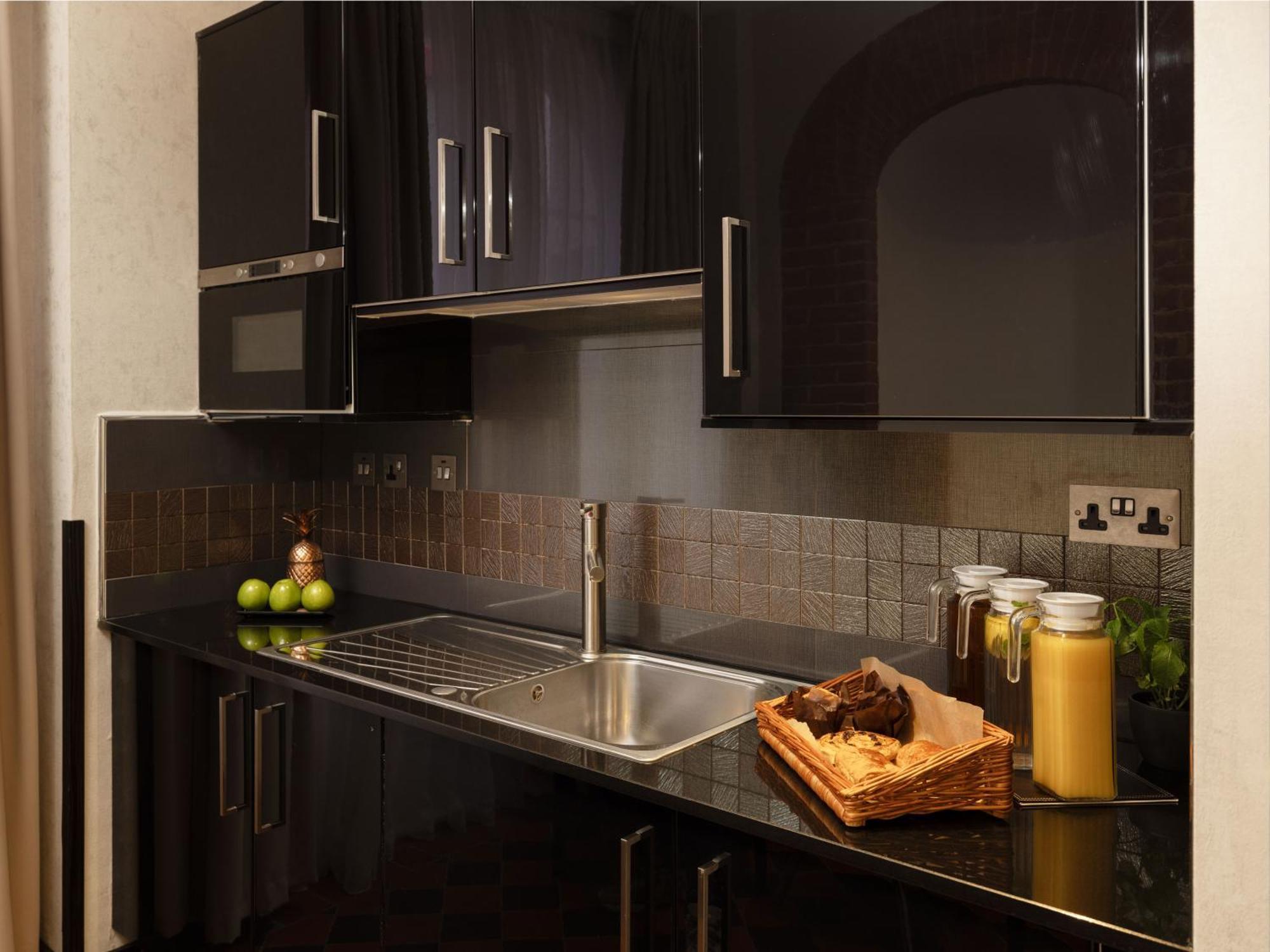 Montcalm Brewery Townhouse Hotel Londra Exterior foto The photo shows a modern kitchen with sleek black cabinetry and a glossy finish. The kitchen features a stainless steel sink with a contemporary faucet, set against a dark, textured countertop. Above the counter, there are cabinets that match the cou
