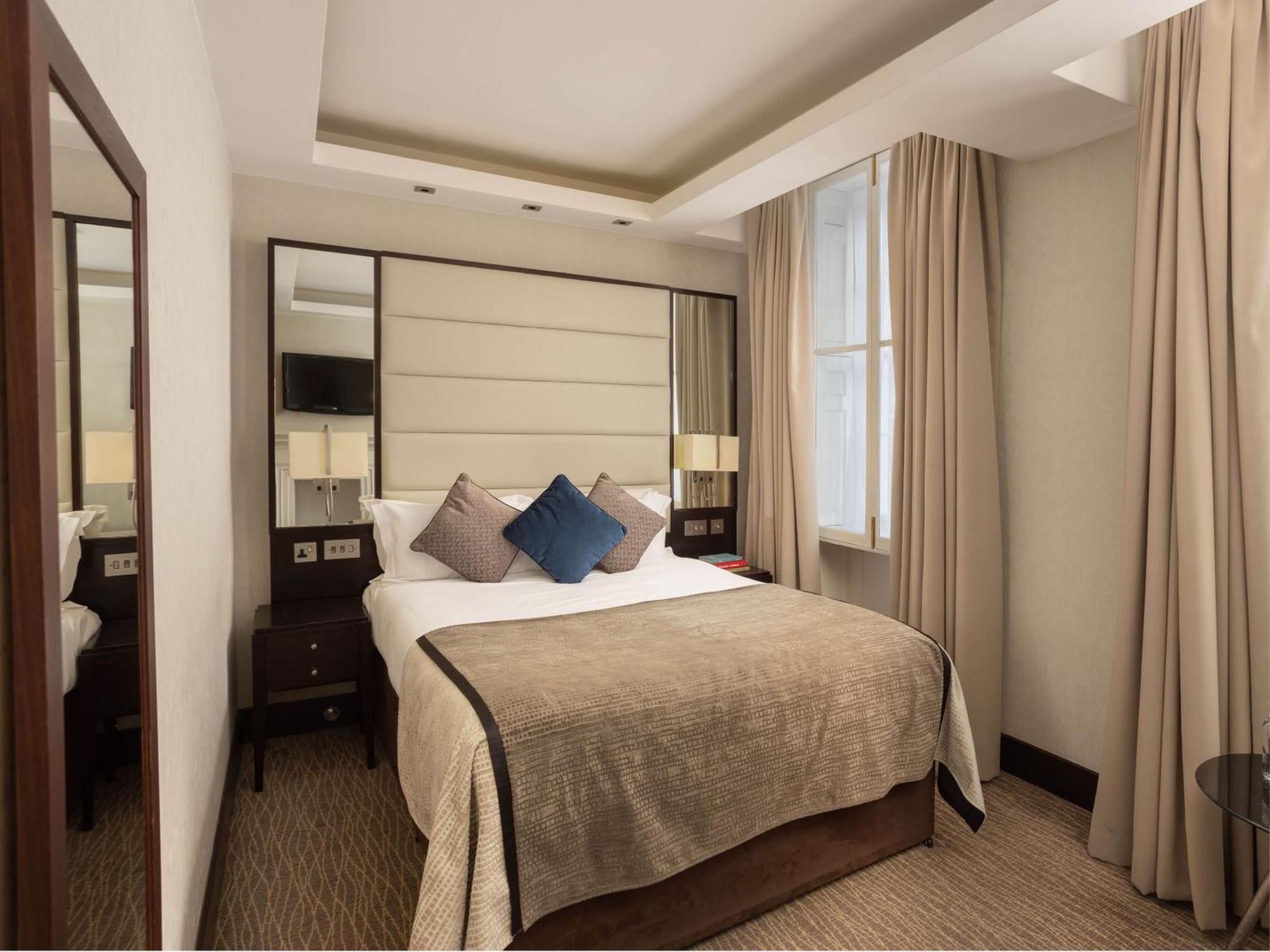 Montcalm Brewery Townhouse Hotel Londra Exterior foto The photo shows a cozy hotel room with a bed as the focal point. The bed is made with neutral-colored linens and has several pillows, including a decorative blue one. There are bedside tables on either side of the bed, each with a lamp. A large mirro