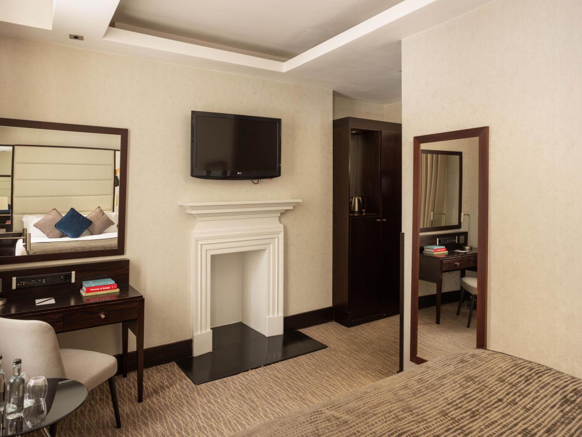 Montcalm Brewery Townhouse Hotel Londra Exterior foto The photo depicts a stylish hotel room. It features a double bed, a large flat-screen TV mounted on the wall, and a decorative fireplace. There is a wooden desk with a chair beside it, as well as a mirror hanging on the wall. The decor is modern and 