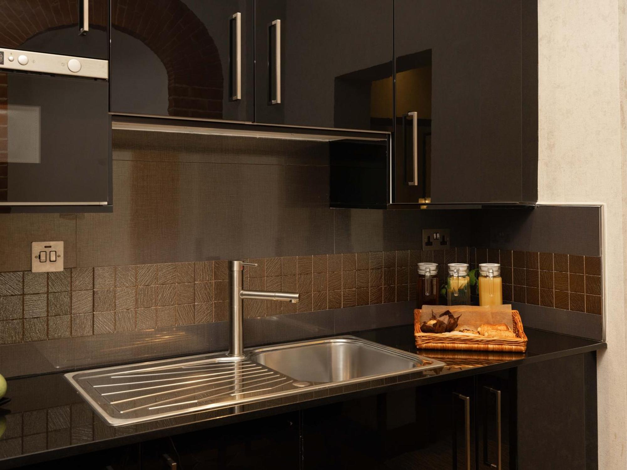 Montcalm Brewery Townhouse Hotel Londra Exterior foto The photo shows a modern kitchen with a sleek design. It features dark cabinetry with a glossy finish and stainless steel handles. There is a stainless steel sink with a simple faucet, and a countertop made of black material. Above the sink, there ar