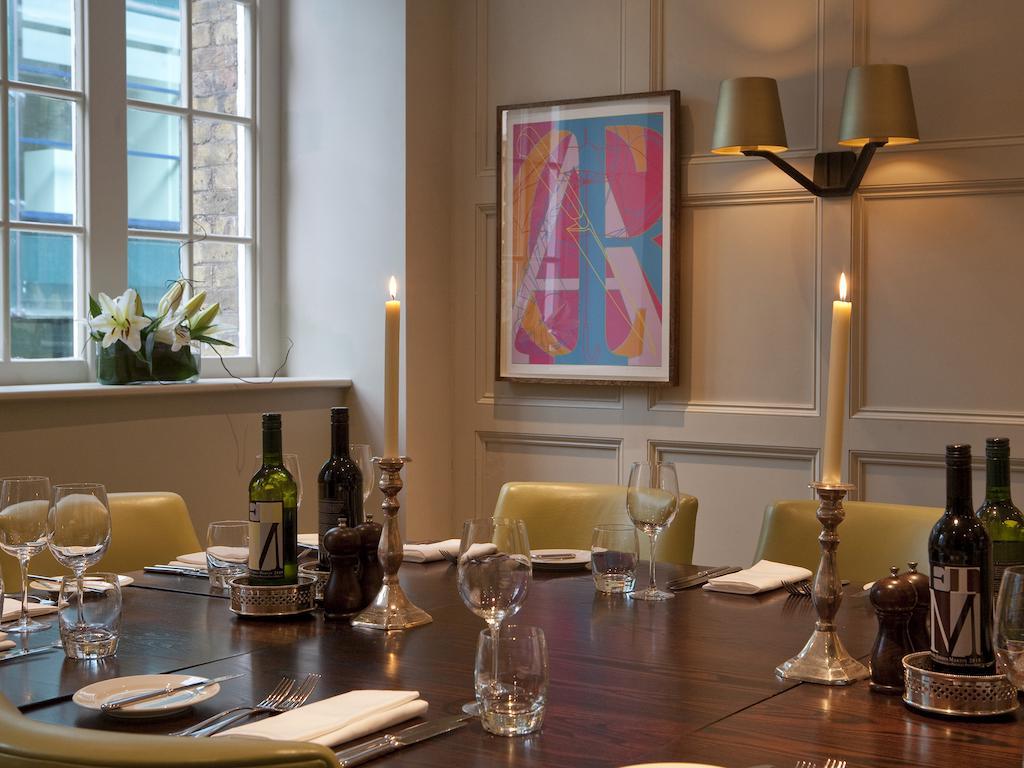 Montcalm Brewery Townhouse Hotel Londra Exterior foto The photo shows an elegantly set dining room with a large wooden table surrounded by several chairs. The table is adorned with neatly arranged utensils, glasses, and decorative items. There are two tall candlesticks with candles and several bottles o