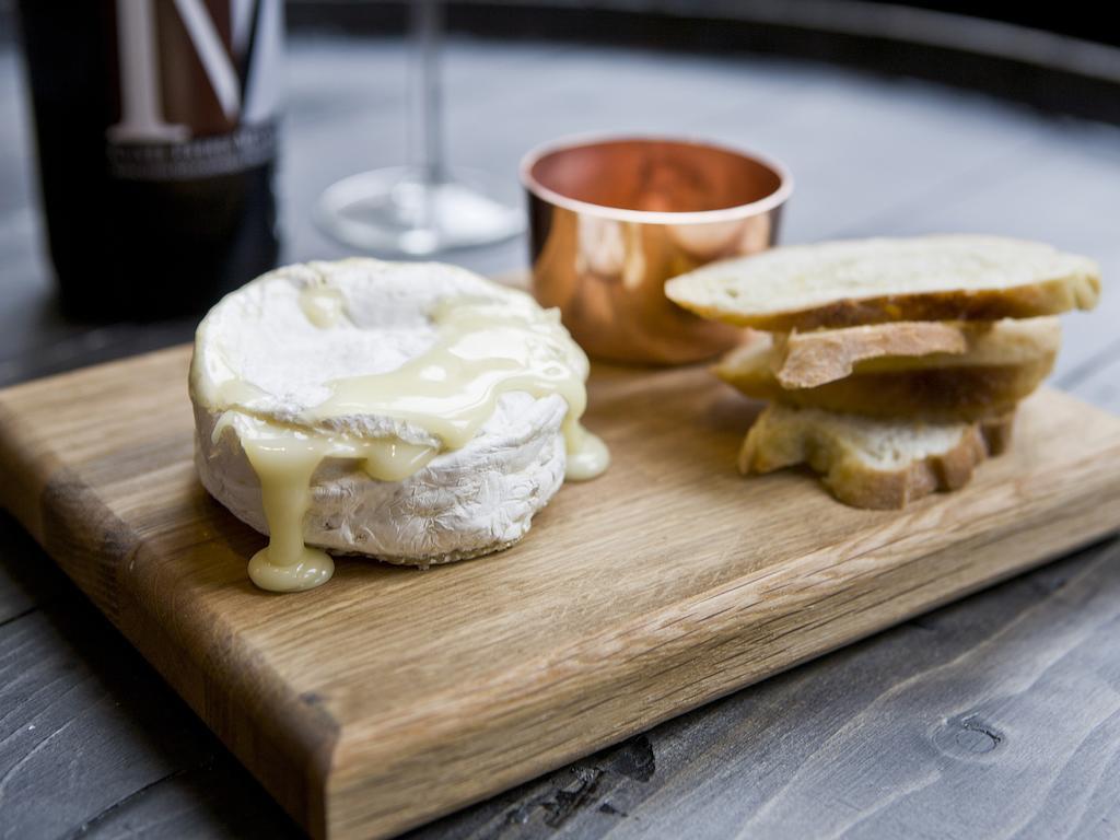 Montcalm Brewery Townhouse Hotel Londra Exterior foto The photo features a wooden serving board with several items. There is a round cheese, likely Brie or a similar soft cheese, that appears to be melting and dripping slightly. Next to the cheese, there is a small copper cup that might contain a sauce 