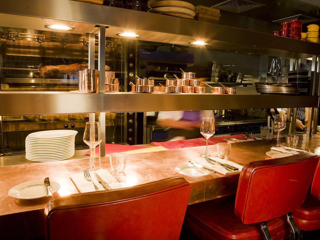 Montcalm Brewery Townhouse Hotel Londra Exterior foto The photo shows a restaurant interior featuring a bar or counter area. There are red chairs arranged around a copper-topped table where dining utensils and plates are set. Above the counter, there are shelves displaying various cooking pots and kitch