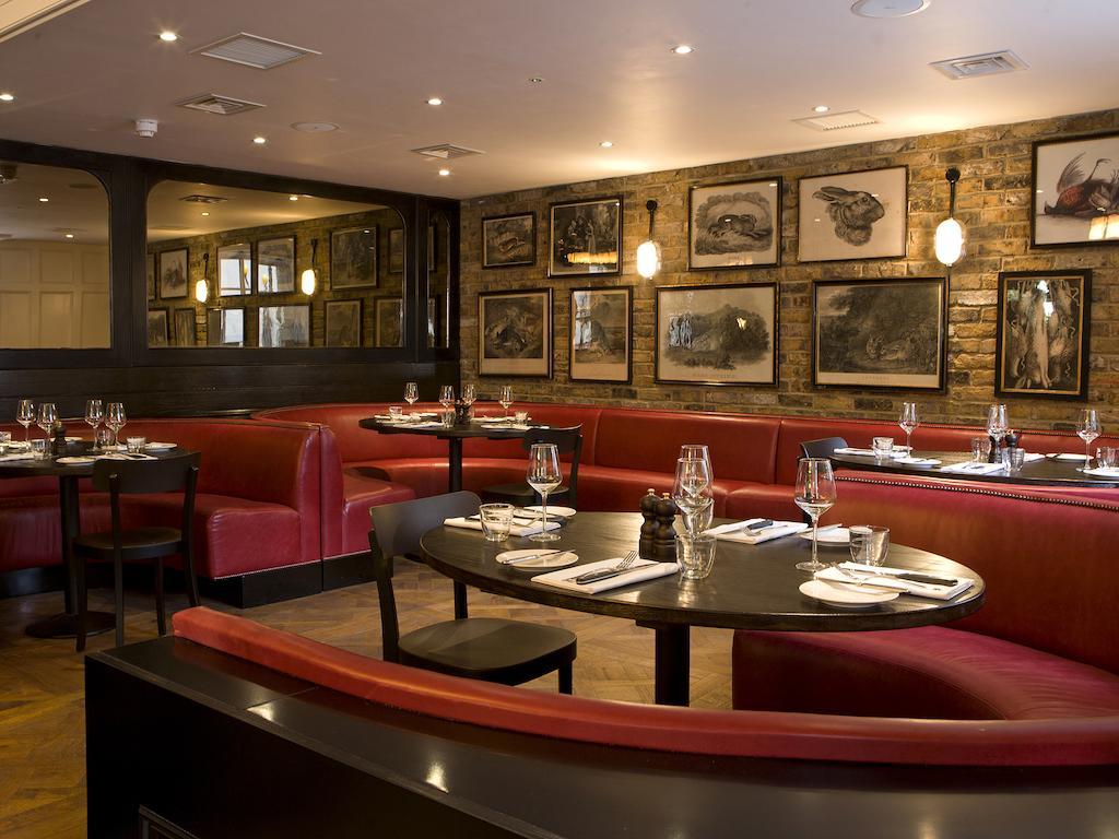 Montcalm Brewery Townhouse Hotel Londra Exterior foto The photo depicts an elegant restaurant interior. There are curved red booths along the walls, creating a cozy seating arrangement. The tables are round and set with white plates and glassware, indicating a prepared dining area. The walls feature a n