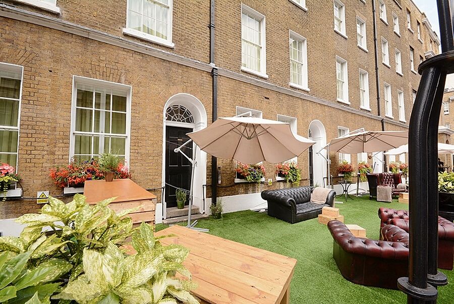 Montcalm Brewery Townhouse Hotel Londra Exterior foto The photo depicts an outdoor area of a building with a brick facade. There are several large windows visible, along with a wooden door. The setting features outdoor furniture, including couches in a dark leather finish and wooden tables. Large umbrel